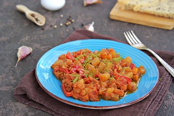 Vegetable ratatouille or stew of zucchini, sweet pepper, carrots and tomato on a blue plate on a dark brown concrete background. Vegetarian food. Autumn harvest. Thanksgiving Day.