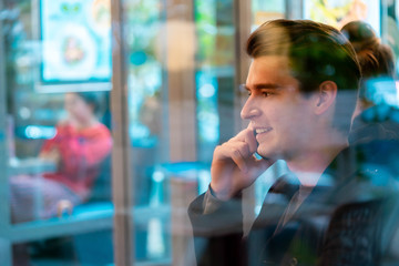 Young handsome man talking by mobile phone in cozy cafe. View from window.