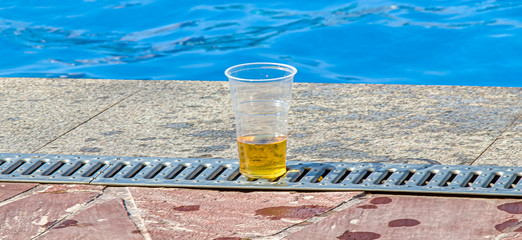 Fototapeta na wymiar Plastic glass with beer on the edge of the pool