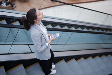 Young businesswoman on the escalator and a phone in her hands. In the office or business center.