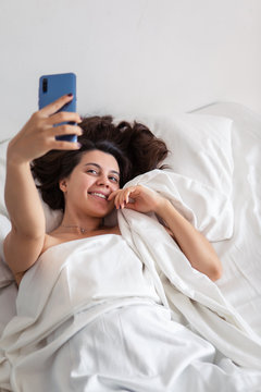 woman laying in bed taking selfie on the phone