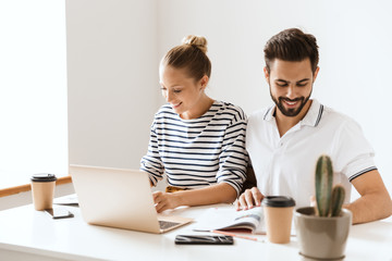 Pleased young loving couple friends man and woman sitting at the table indoors using laptop computer reading book.