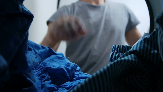 A man opens the door of the washing machine and load the clothes into it - View from inside