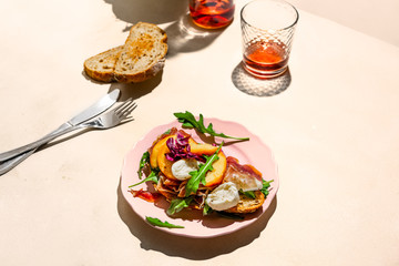 Parma ham, mozzarella and peaches sandwich on a plate, some bread and rose wine shot with hard light