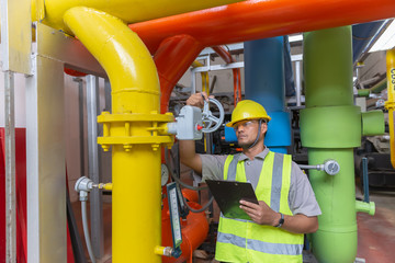 Asian engineer wearing glasses working in the boiler room,maintenance checking technical data of heating system equipment,Thailand people