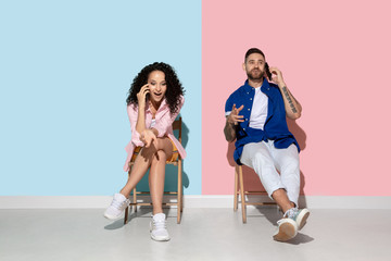 Naklejka premium Young emotional caucasian couple in bright casual clothes posing on pink and blue background. Concept of human emotions, facial expession, relations, ad. Woman and man talking on the phone, smartphone