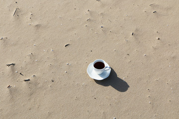 A cup of coffee stands on the sandy seashore