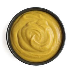 Mustard sauce in dark ceramic bowl isolated on white background. Top view