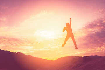 Happy man jumping at top of mountain with sunset sky abstract background.