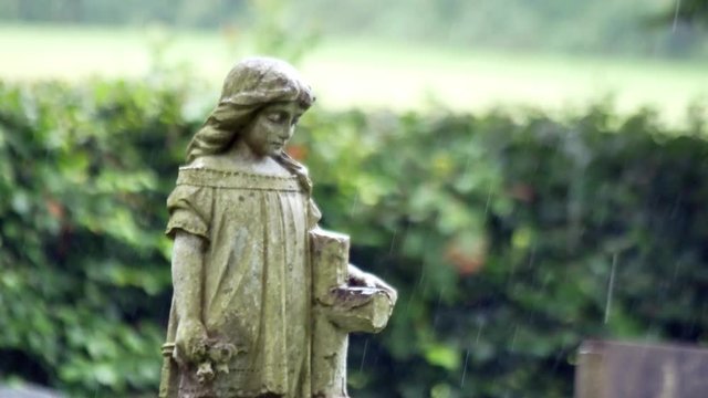 Child angel granite headstone in rainy cemetery burial grounds. Sorrowful praying statue.