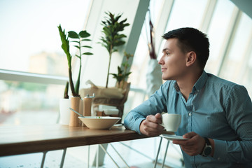 young handsome smiling businessman drinking his hot coffee and eating salad for lunch during break at trendy cafe near office