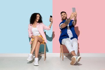 Fototapeta premium Young emotional caucasian couple in bright casual clothes posing on pink and blue background. Concept of human emotions, facial expession, relations, ad. Woman and man make selfie, smile, laught.