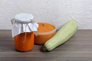 Homemade seasonal preparations. In the bank squash caviar. Nearby lies a fresh zucchini and zucchini caviar in an open container. The neck of the can is wrapped in paper and tied with a rope.