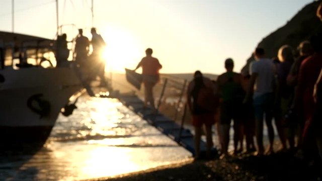 Unrecognizable people board a boat, ferry or ship on the shore of the sea, ocean, river. Sunset. Unfocused background.