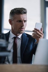 selective focus of surprised man holding smartphone