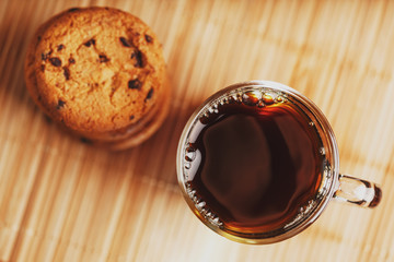 Oatmeal cookies with chocolate pieces and a mug of aromatic black tea in on a bamboo substrate, Low contrast.