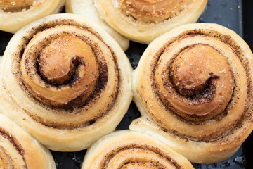 Twisted buns made from yeast dough with cinnamon, cane sugar and coconut chips on a black baking sheet, close-up