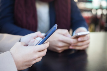 Close-up of two people hands using smartphone outdoors