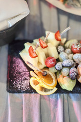 Fruit sliced on a stylish plate. Pineapple, pear, orange, apple, grape, wild strawberry.