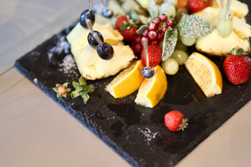 Fruit sliced on a stylish plate. Pineapple, pear, orange, apple, grape, wild strawberry.