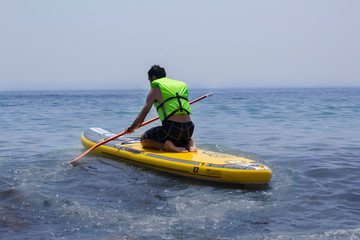Fototapeta na wymiar Man practicing paddle surf kneeling on the board