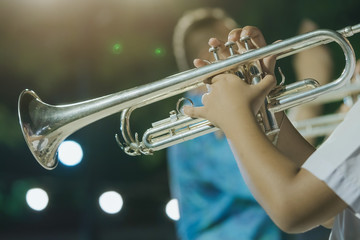Male student with friends blow the trumpet with the band for performance on stage at night. © JinnaritT