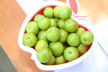 green sour plums in the plate, plums on the wooden floor waiting for pregnant . Green sour plums in the apple plate, plum pictures on the white ground .