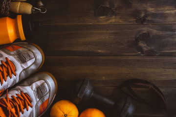 Fitness, healthy and active lifestyles background concept, Top view image of old sport shoes, jumping rope, dumbbells, bottle of water,sport glasses and orange  on dark wooden floor.