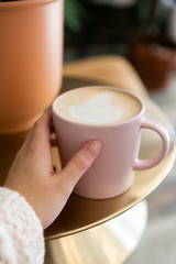 Close up of woman holding coffee latte, chunky sweater, hipster coffee shop, hand on pink coffee cup