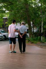 Fototapeta premium Young man take care senior man to walk. Old senior family concept. view from the back
