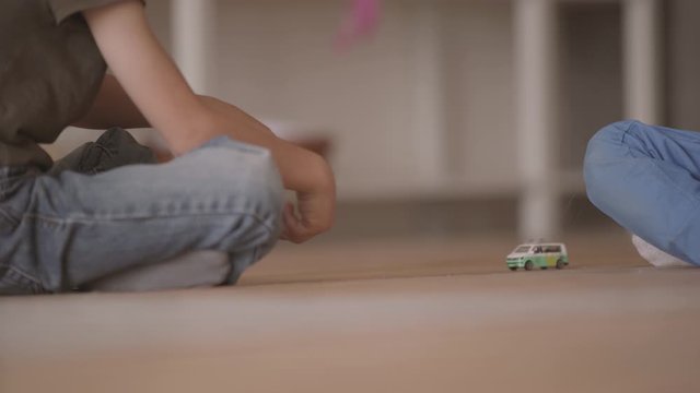 Two unrecognized ittle boys sitting on the floor playing with the toy car sitting on the floor at home. Siblings spending time at home. Happy family, carefree childhood.
