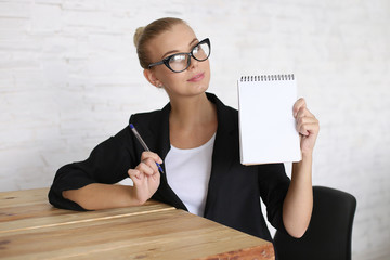 The girl sits at a table with a notebook, in a jacket and glasses. Makes notes for work. Copy space.