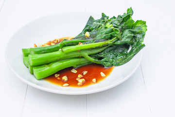 Fried kale, oyster oil with fried garlic in a plate On a white wood table background
