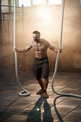 Strong young man screaming while making exercise with crossfit rope.