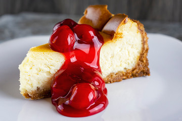 A slice of New York style cheesecake with cherry sauce.  Close up view on a white plate.  Neutral blurry background.