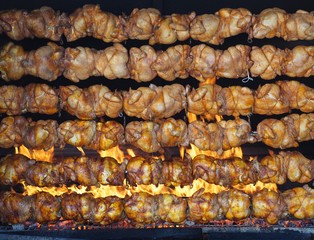 Roasted chickens grilled on rotating spit over the flames. Rotisserie.