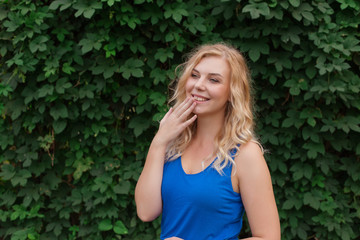 Beautiful young girl smiles in a blue dress, against a background of hedges of wild grapes. Copy space.