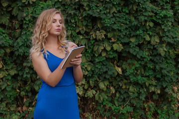 Young beautiful girl on a background of a wall of wild grapes, makes notes in a notebook, an idea has come. Copy space.