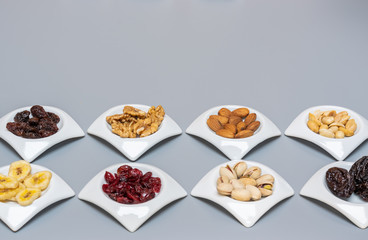 Nuts and dried fruits in white saucers on gray matte background,selective focus and copy space.