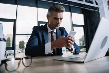 selective focus of man using smartphone near smartphone and glasses