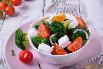 Light salad with broccoli, cherry tomatoes and feta cheese in a white ceramic bowl