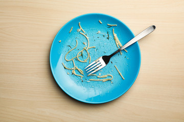 Dirty plate with food leftovers and fork on wooden background, top view
