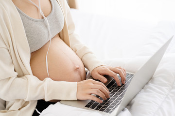 Naklejka premium Closeup at hands of Asian pregnant mother looking for music on Laptop will help to feel relax, happy and have a positive effect on unborn child. Online shop related to children accessories on social.