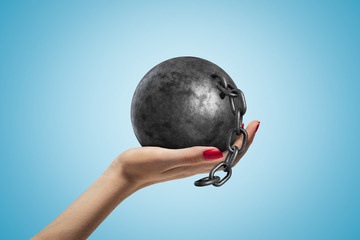 Side closeup of woman's hand facing up and holding black ball and chain on light blue gradient...