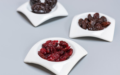 Food,taste and snack concept: dried red cranberries in small white saucers on gray matte background, selective focus.
