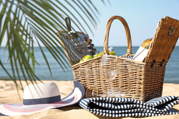 Wicker picnic basket with products, blanket and hat on sunny beach