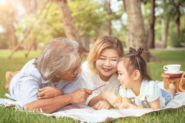 Grandmother,Grandfather and grand daughter enjoying sunny garden holiday together, outdoors space, leisure lifestyle,happy teaching with flare light sky in park.