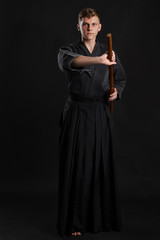 Kendo guru wearing in a traditional japanese kimono is practicing martial art with the shinai bamboo sword against a black studio background.