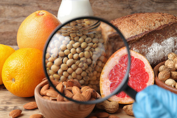 Different products with magnifier focused on jar of soy, closeup. Food allergy concept - obrazy, fototapety, plakaty