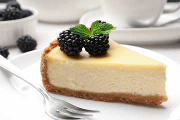 Piece of delicious cheesecake decorated with blackberries on table